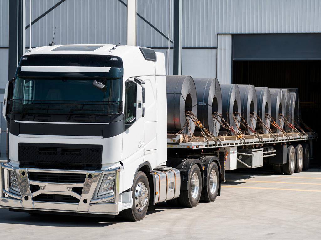 Industrial goods and steel components being loaded onto a white Volvo curtainsider at a supply yard
